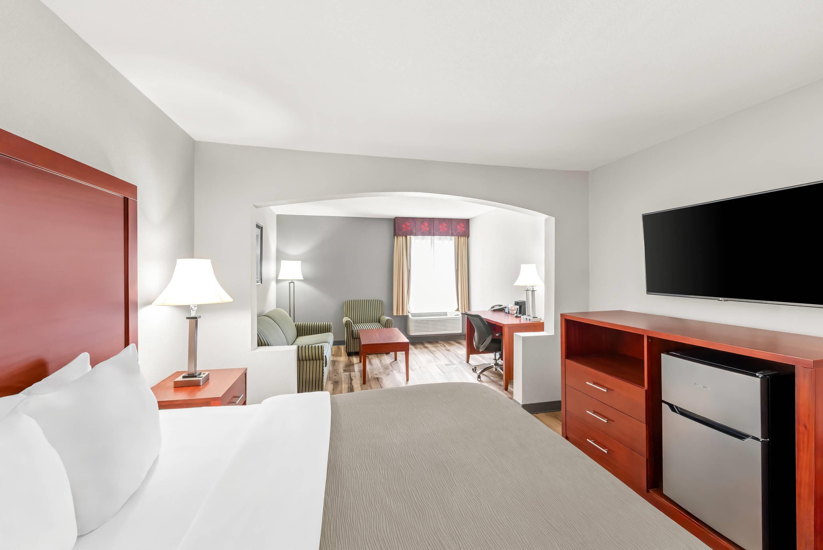 Habitación de hotel con cama, escritorio, silla, televisor y refrigerador.