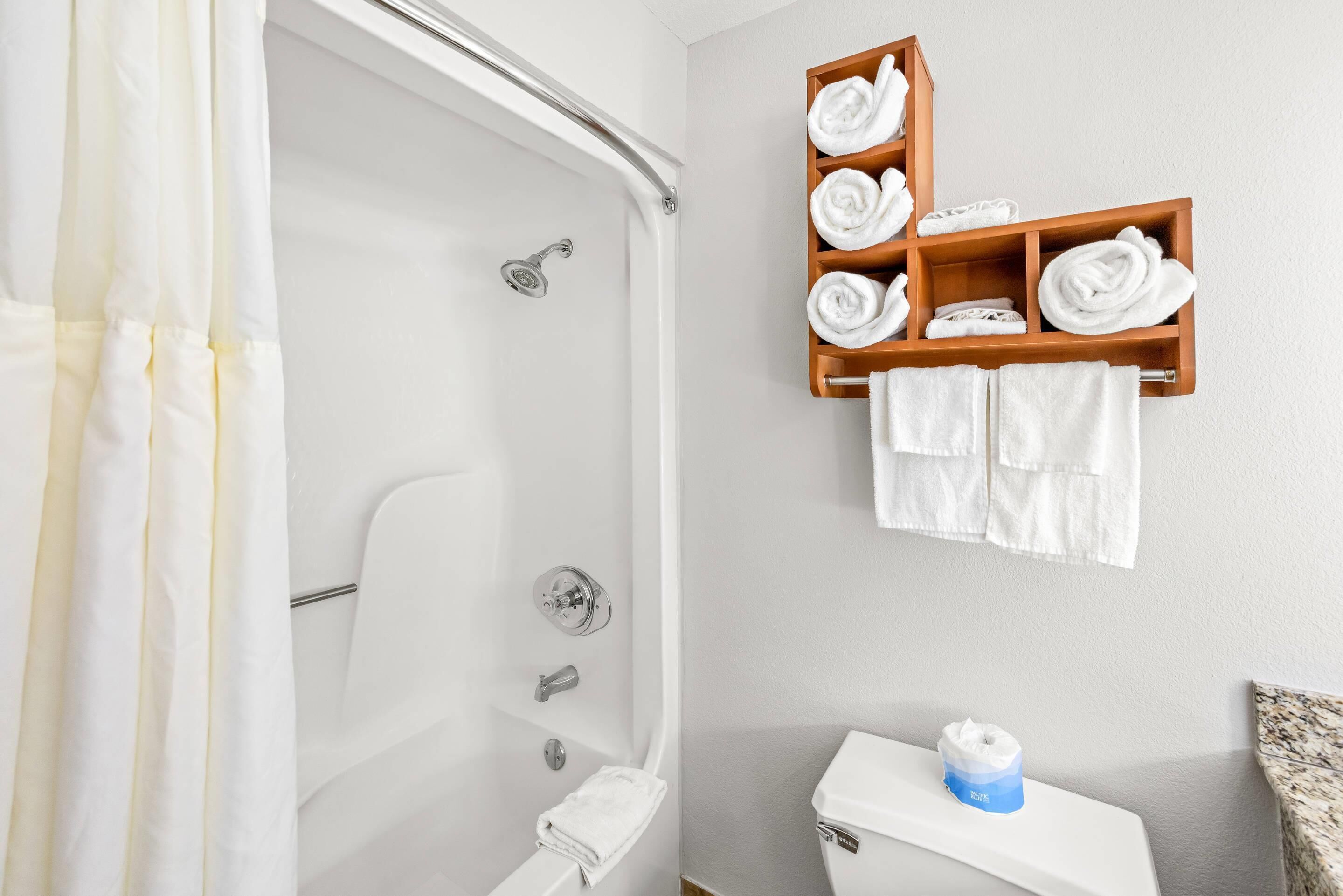 A bathroom with a shower, toilet, and a shelf with towels.
