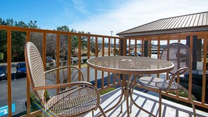 A balcony with a metal table and chairs, overlooking a parking area and trees.