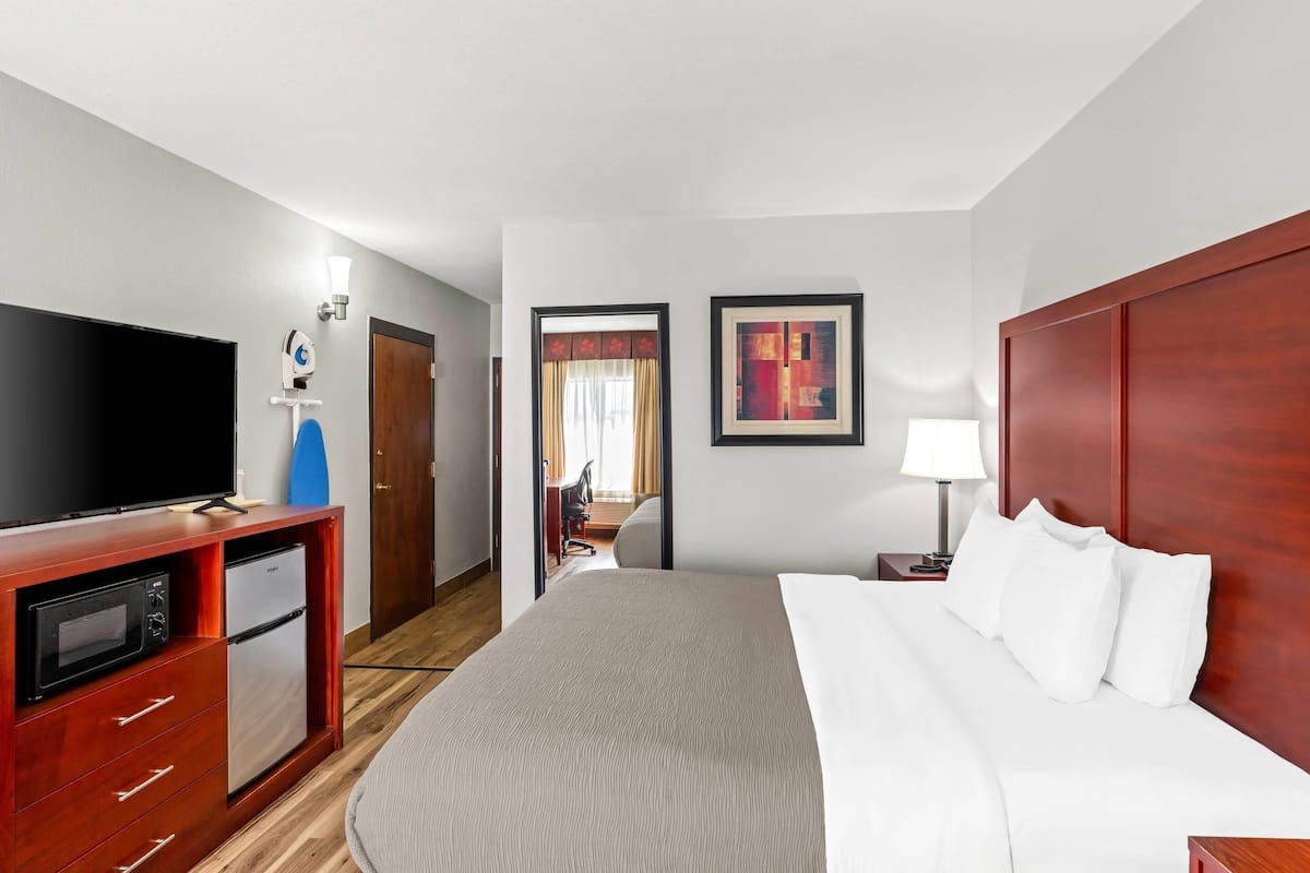 A hotel room with a bed, a TV, a mini-fridge, a desk, and a chair.