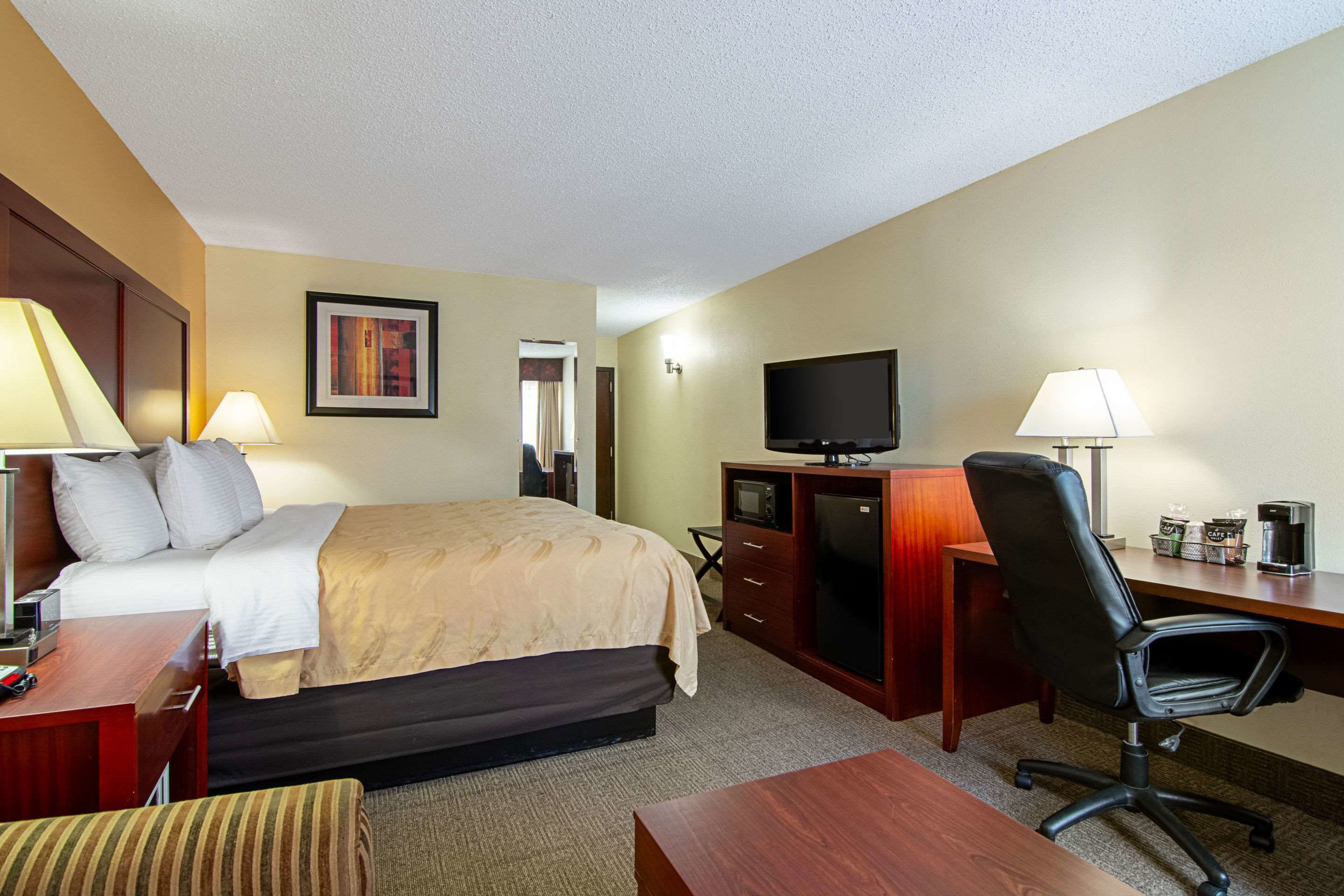 A hotel room with a bed, desk, chair, television, and a small kitchenette area.
