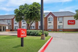 A Red Roof Inn & Suites building with a clear entrance sign, brick facade, and a well-maintained lawn. - Red Roof Inn & Suites Euless - DFW Airport Southwest (Euless)