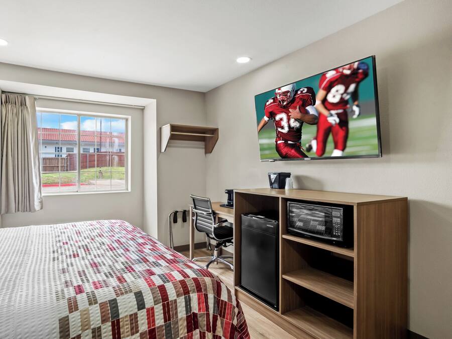 Une chambre d’hôtel avec un lit, un bureau, une télévision et une fenêtre avec des rideaux.