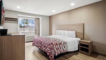 A modern hotel room with a large bed, a bedside table, a desk, and a window with curtains.