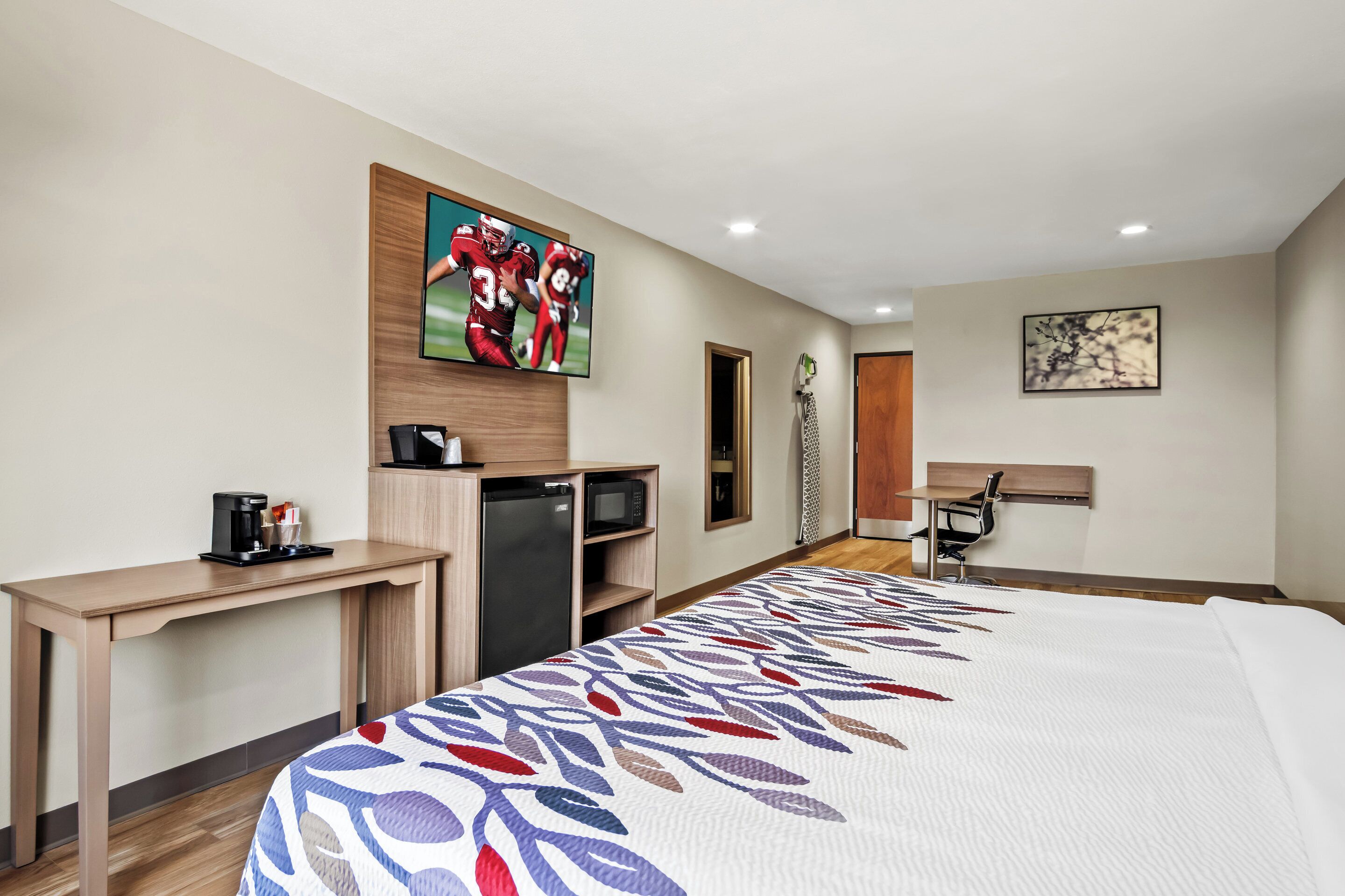Una camera d'albergo con un letto, una scrivania, un forno a microonde, una macchina del caffè, una TV e un quadro appeso al muro.