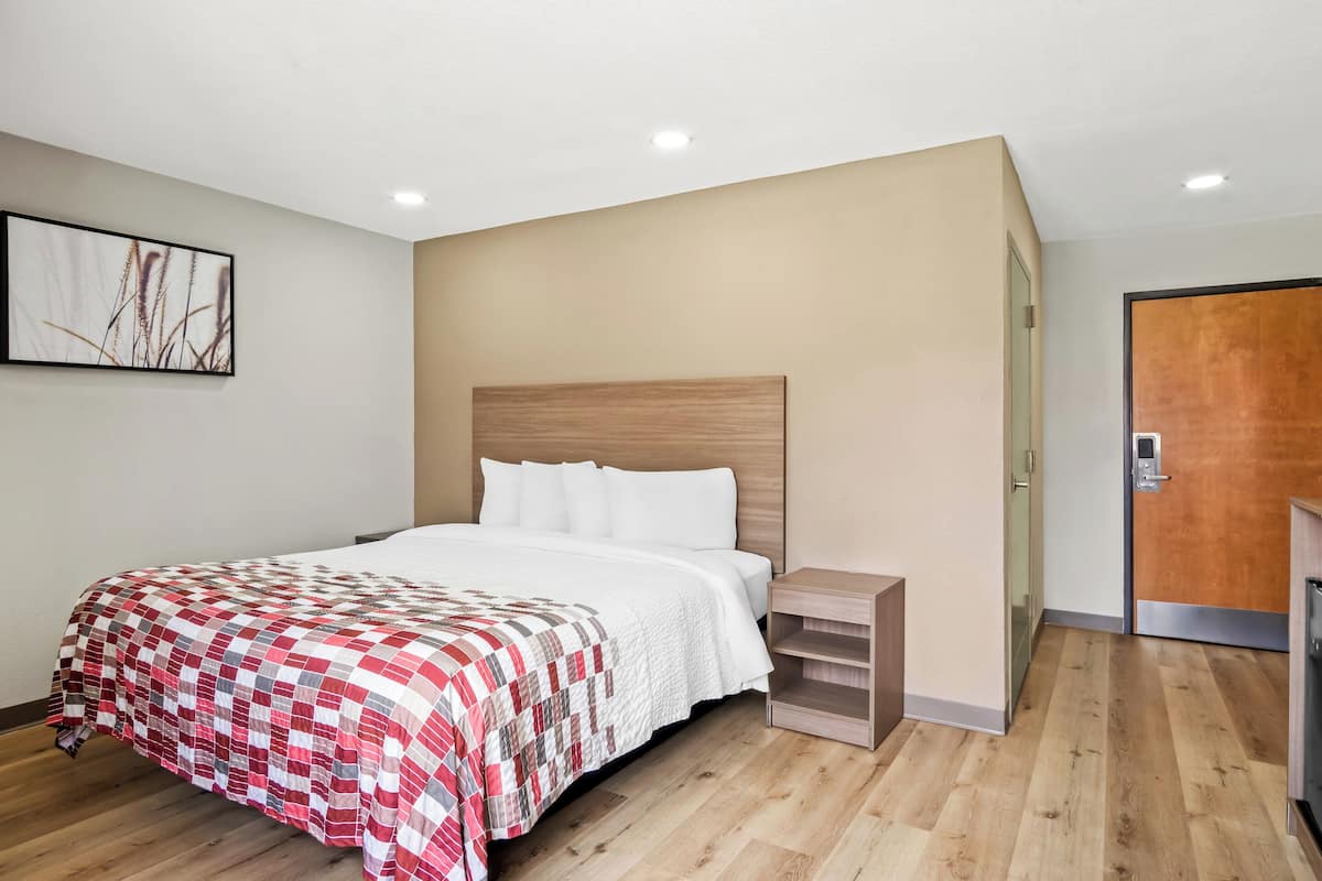 Una habitación de hotel moderna con suelo de madera, una cama con colcha roja y blanca, una mesita de noche y un cabecero de madera.