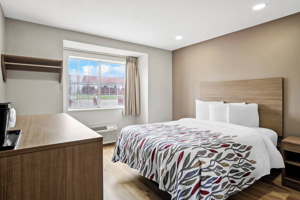 Una habitación de hotel con cama, escritorio, ventana con cortinas y vista a un área cercada.