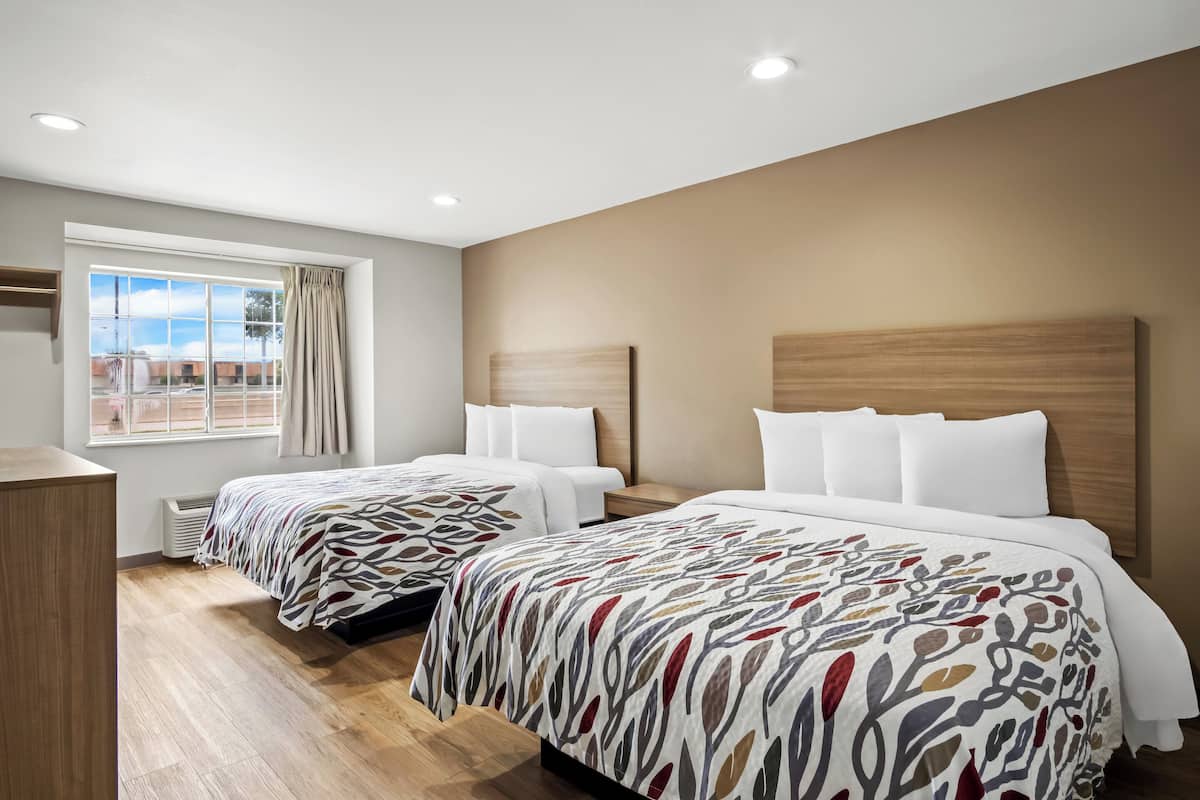 Habitación de hotel con dos camas, un ventanal grande con cortinas, cabecera de madera y calefacción integrada.