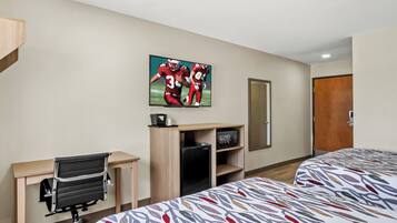 A hotel room with a bed, a desk with a chair, a refrigerator, a microwave, and a television on the wall.