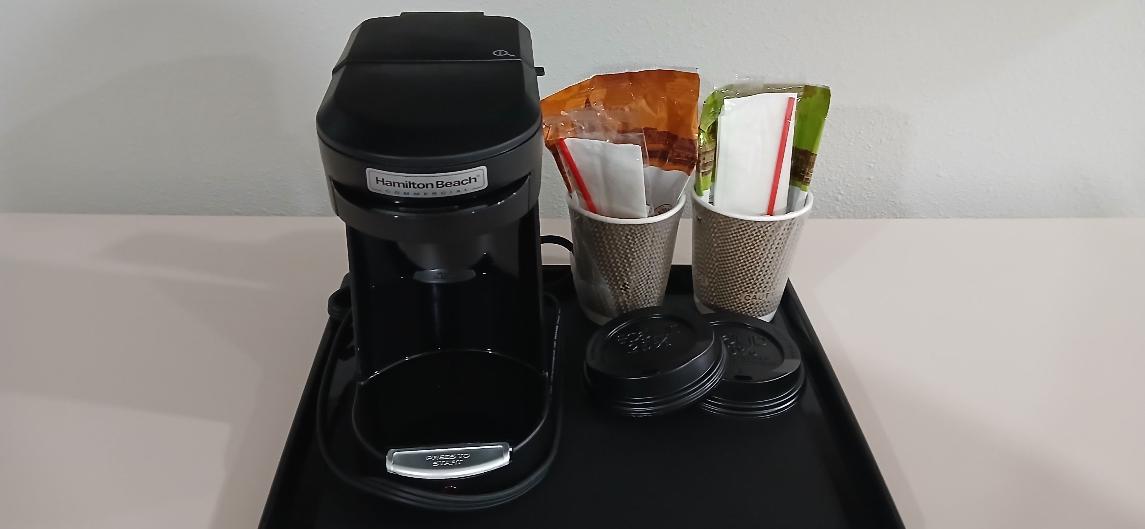 A Hamilton Beach commercial coffee maker on a black tray with two paper filters and a coffee pot.