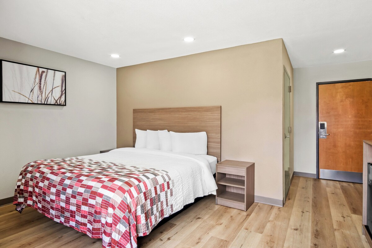 Ein modernes Hotelzimmer mit Holzboden, einem Bett mit rot-weiß gestreckter Bettdecke, einem Nachttisch und einem Holzkopfteil.