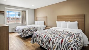 Ein Hotelzimmer mit zwei Betten, einem großen Fenster mit Vorhängen, einem hölzernen Kopfteil und einer fest installierten Heizung.
