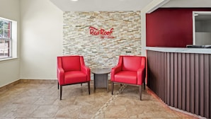 A reception area with two red chairs, a stone wall with a Red Roof Inn & Suites sign, and a modern reception desk. - Red Roof Inn & Suites Euless - DFW Airport Southwest (Euless)
