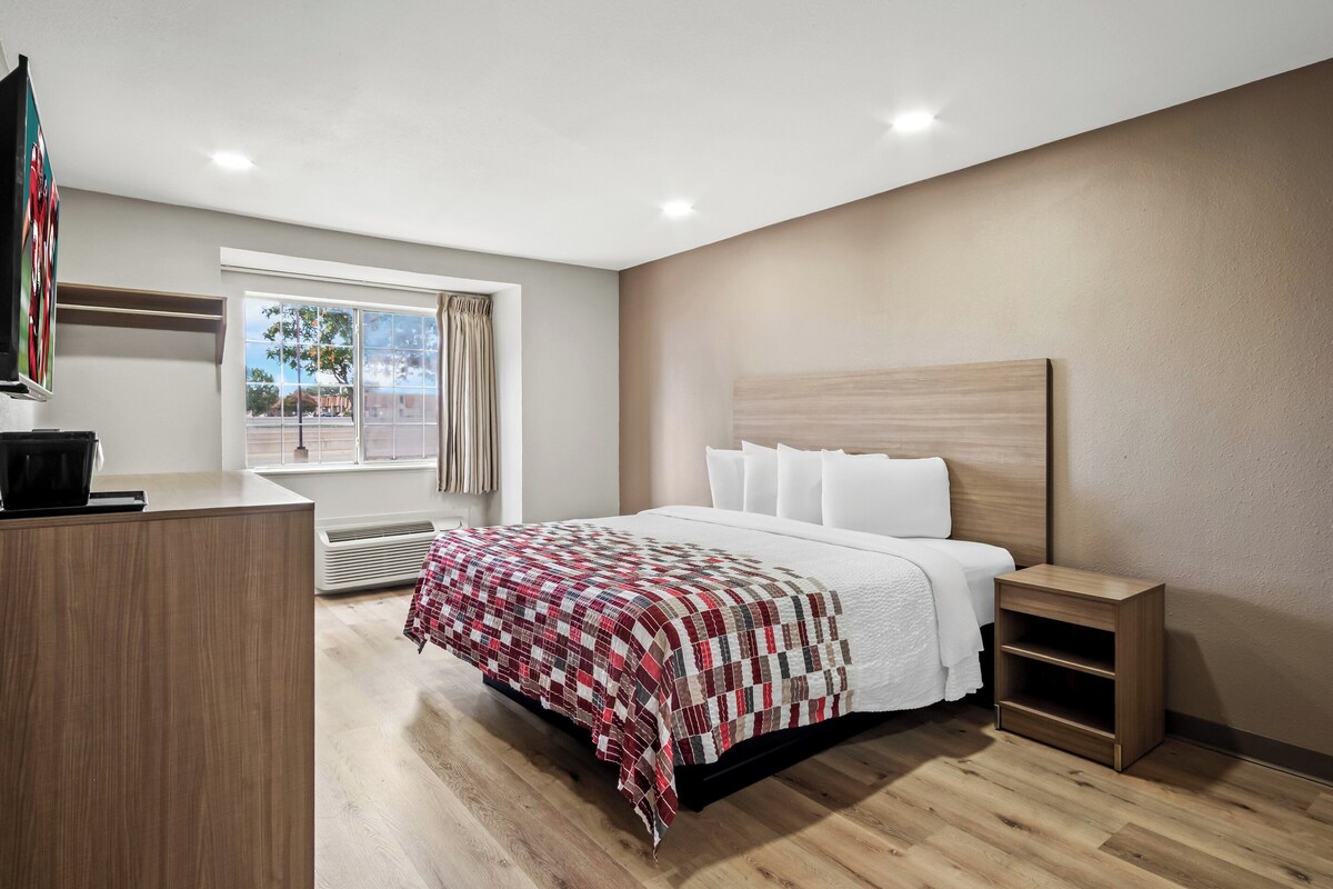 Ein modernes Hotelzimmer mit einem großen Bett, einem Nachttisch, einem Schreibtisch und einem fensterbepflanzten Fenster.