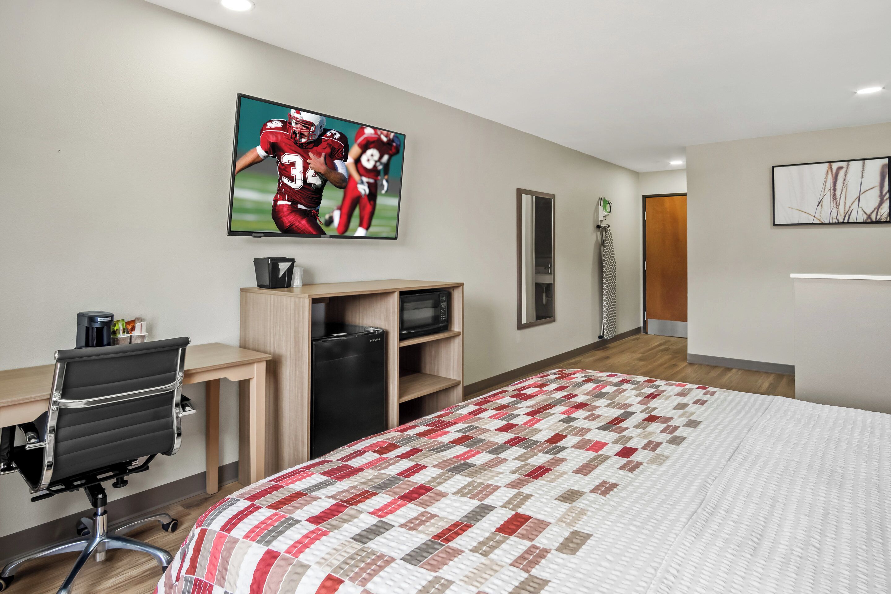 A hotel room with a bed, a desk with a computer, a TV, and a microwave.