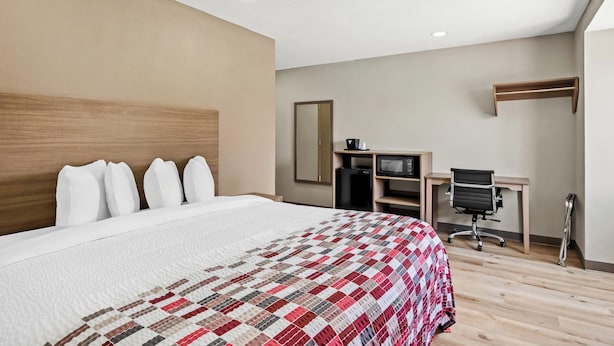 A hotel room with a large bed, a desk with a chair, a microwave, and a small refrigerator. - Red Roof Inn & Suites Euless - DFW Airport Southwest (Euless)