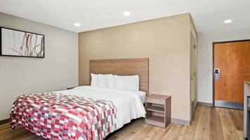A modern hotel room with a wooden floor, a bed with a red and white quilt, a nightstand, and a wooden headboard.