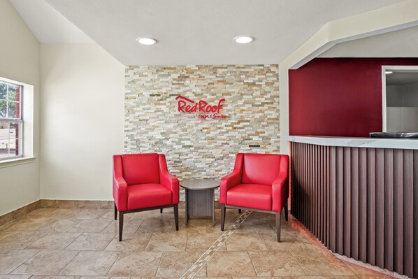 Ein Empfangsbereich mit zwei roten Stühlen, einer Steinwand mit dem Schild Red Roof Inn & Suites und einem modernen Empfangstresen.