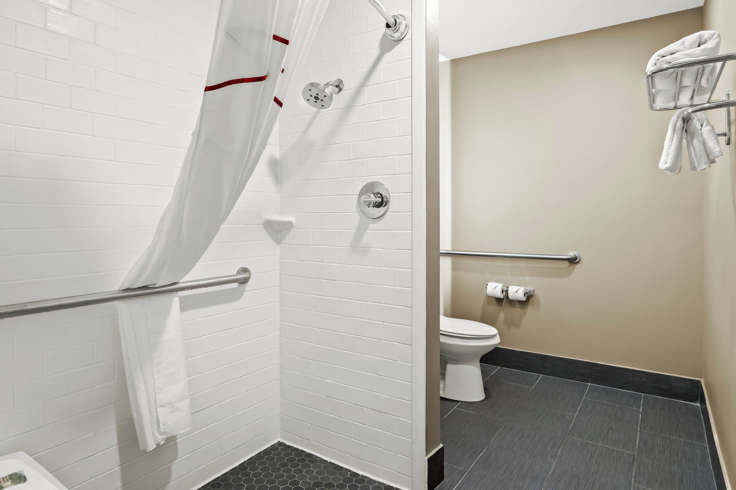 A bathroom with white tiled walls, a shower with a glass door, a toilet, and a towel rack.