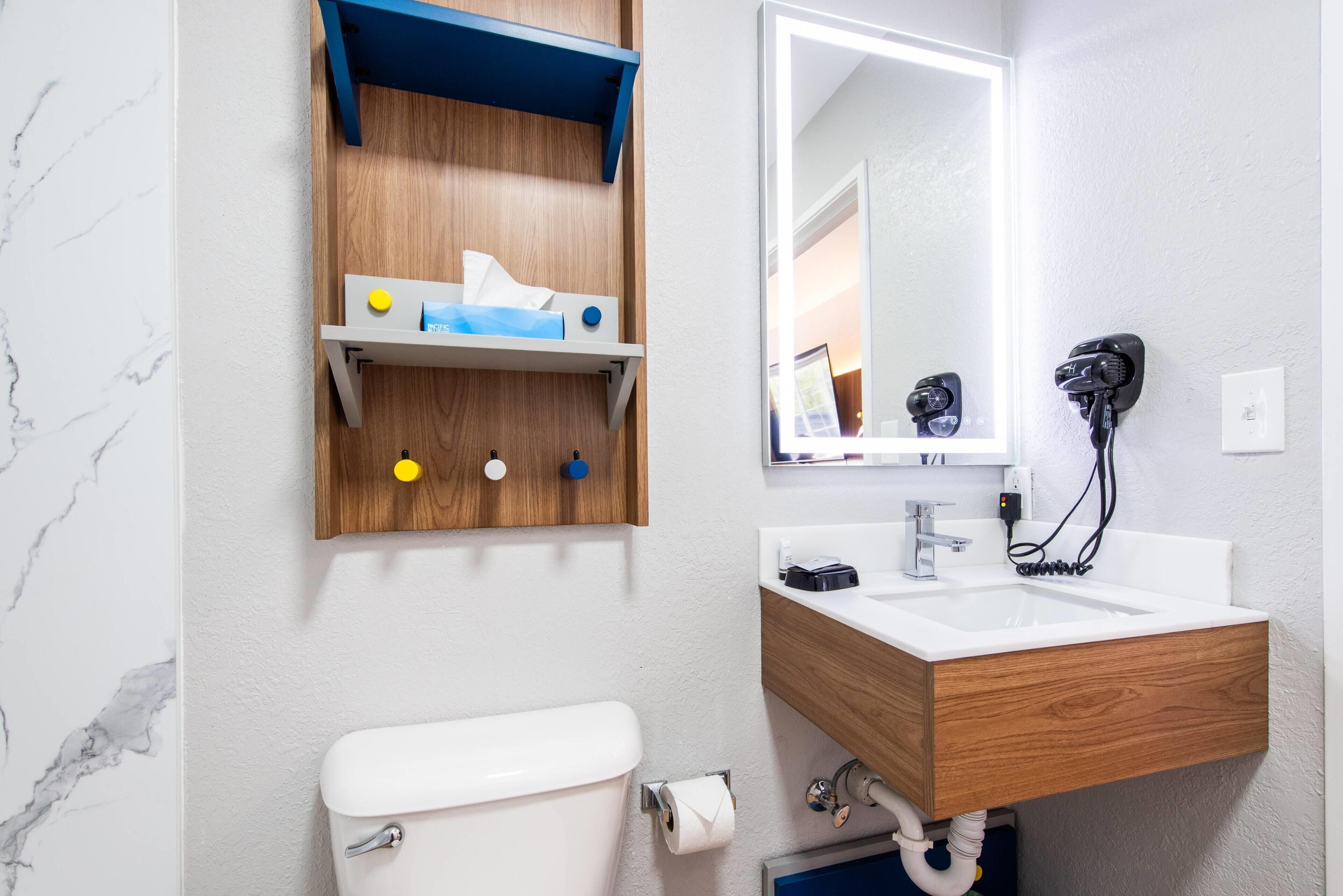 A bathroom with a toilet, sink, mirror, and wooden cabinet with toiletries.