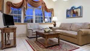 A living room with a beige sofa, a wooden coffee table, a TV on a wooden stand, a large window with curtains, and a mirror on the wall. - Microtel Inn & Suites by Wyndham London (London)