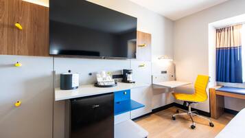 A compact hotel room with a kitchenette, a flat-screen TV, a desk, a chair, and a bed.