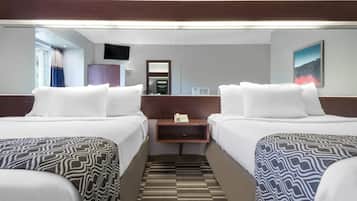 A hotel room with two beds, a bedside table with a telephone, a flat-screen TV mounted on the wall, and a patterned carpet.