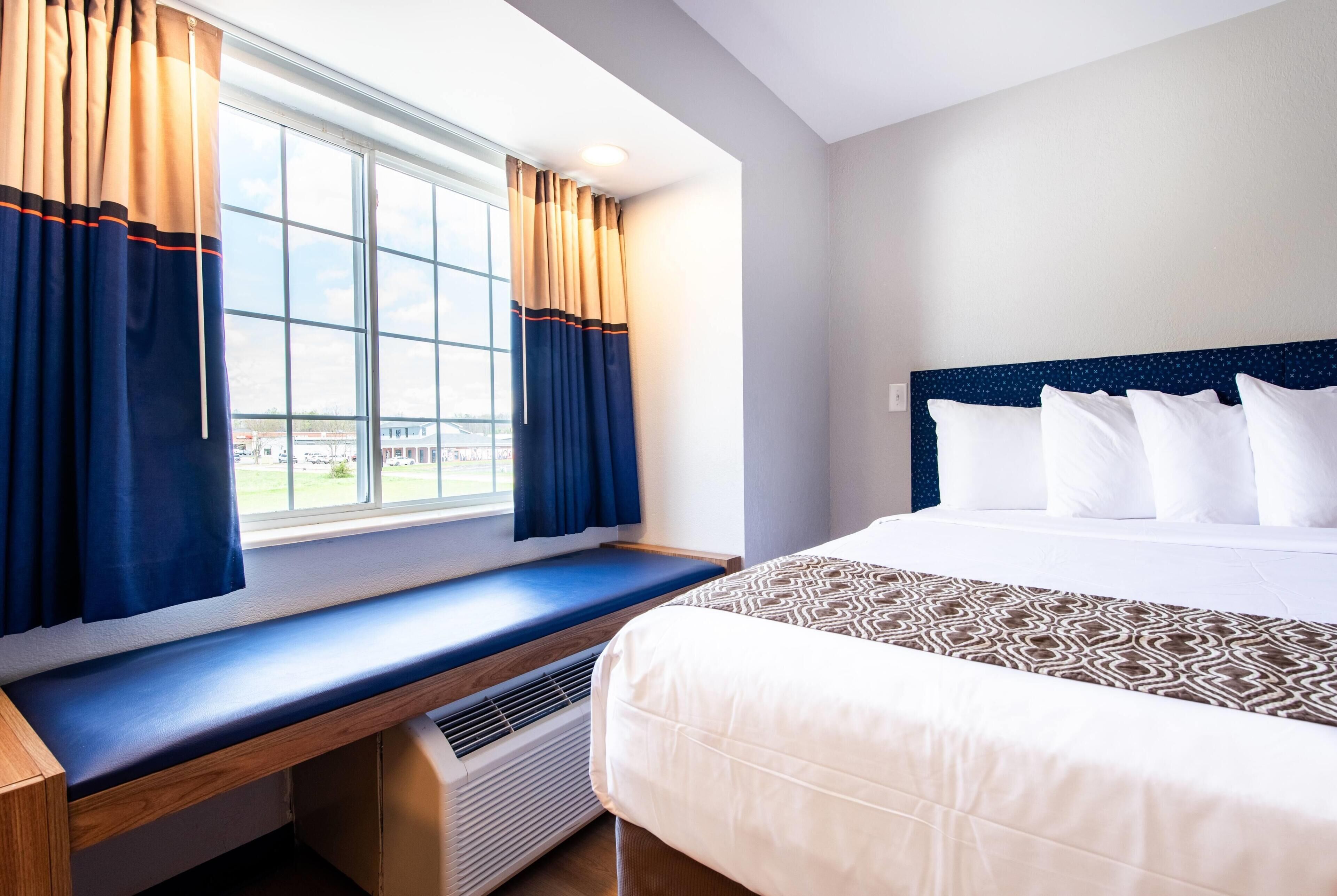 A hotel room with a large bed, a bench by the window, and a view of the outdoors.