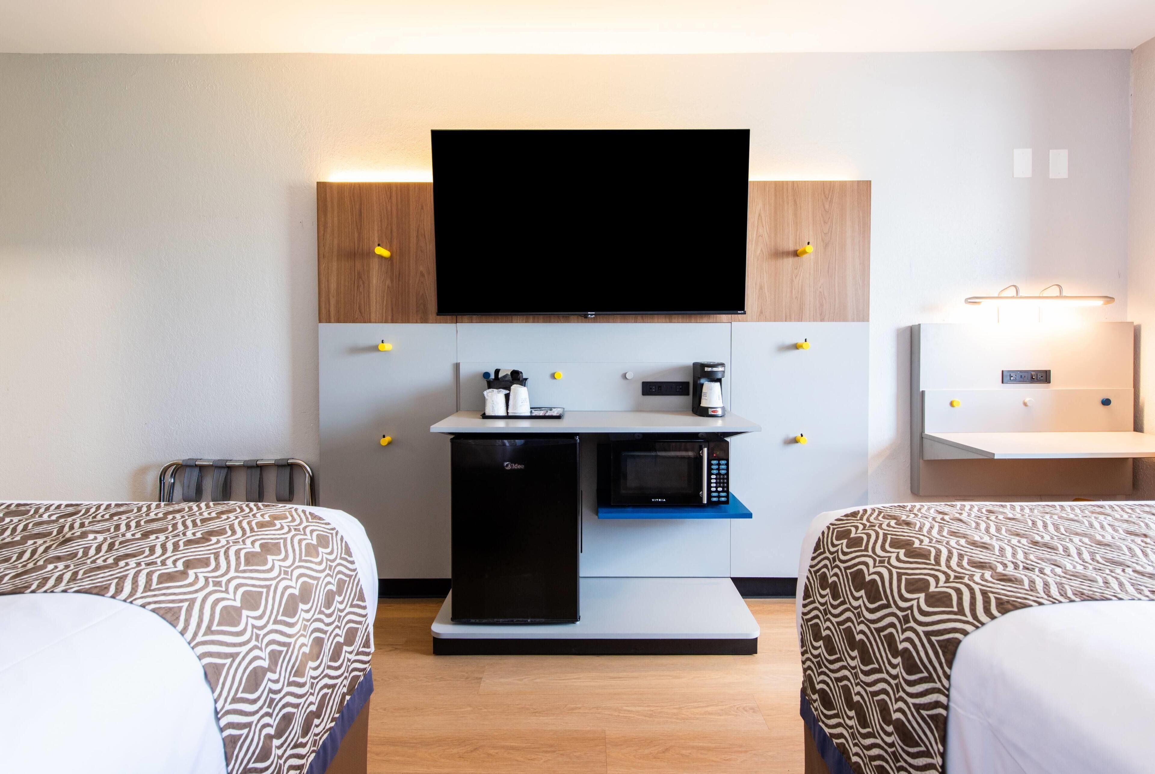 Une chambre d’hôtel avec deux lits, un téléviseur à écran plat, un mini-réfrigérateur, un four à micro-ondes, une machine à café et un petit bureau avec une lampe.