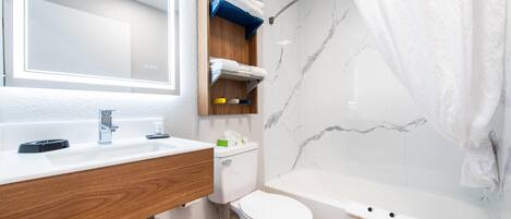 A modern bathroom with a wooden vanity, a white toilet, a bathtub, and a marble wall.