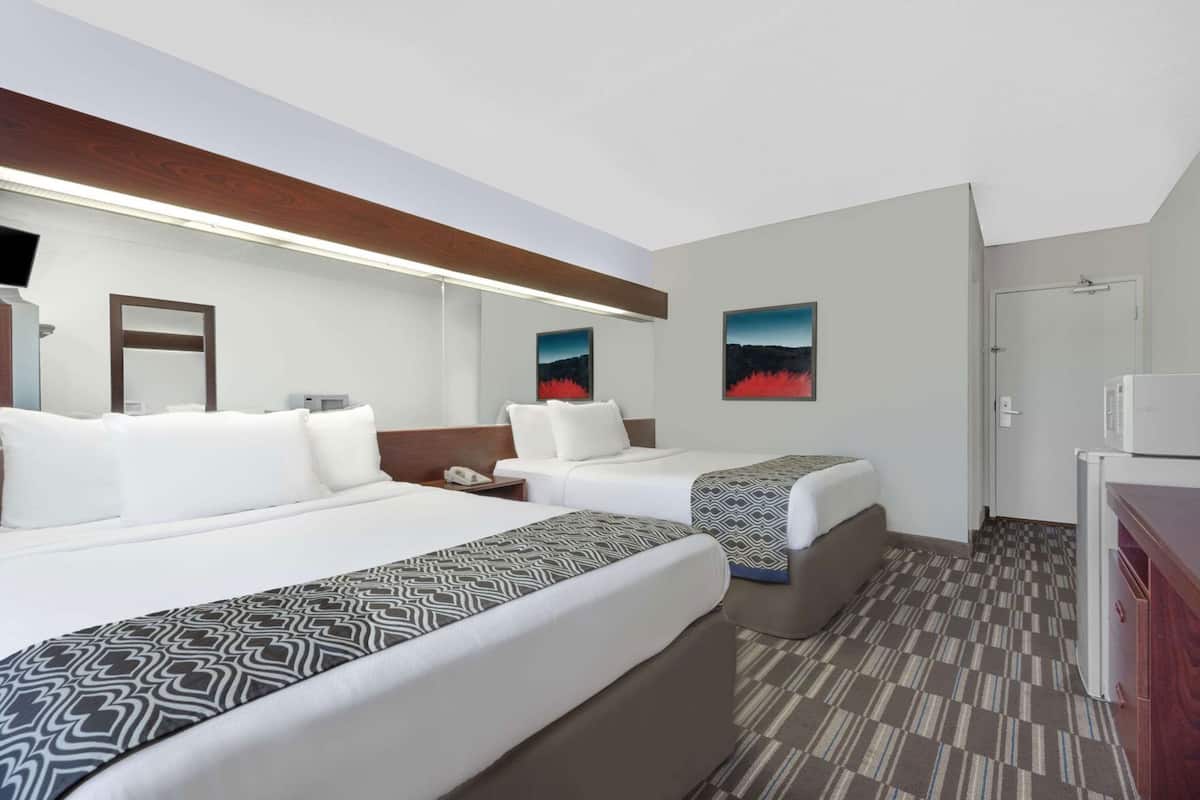 A hotel room with two beds, a desk, a microwave, and artwork on the walls.