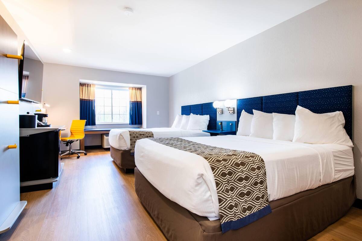 A hotel room with a large bed, a desk, a chair, and a window with curtains.