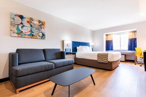 A modern hotel room with a sofa, bed, desk, and artwork on the wall. - Microtel Inn & Suites by Wyndham London (London)