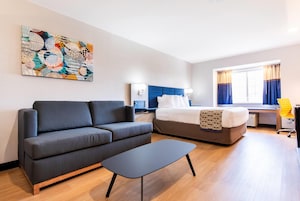 Quarto de hotel moderno com sofá, cama, escrivaninha e obras de arte na parede.