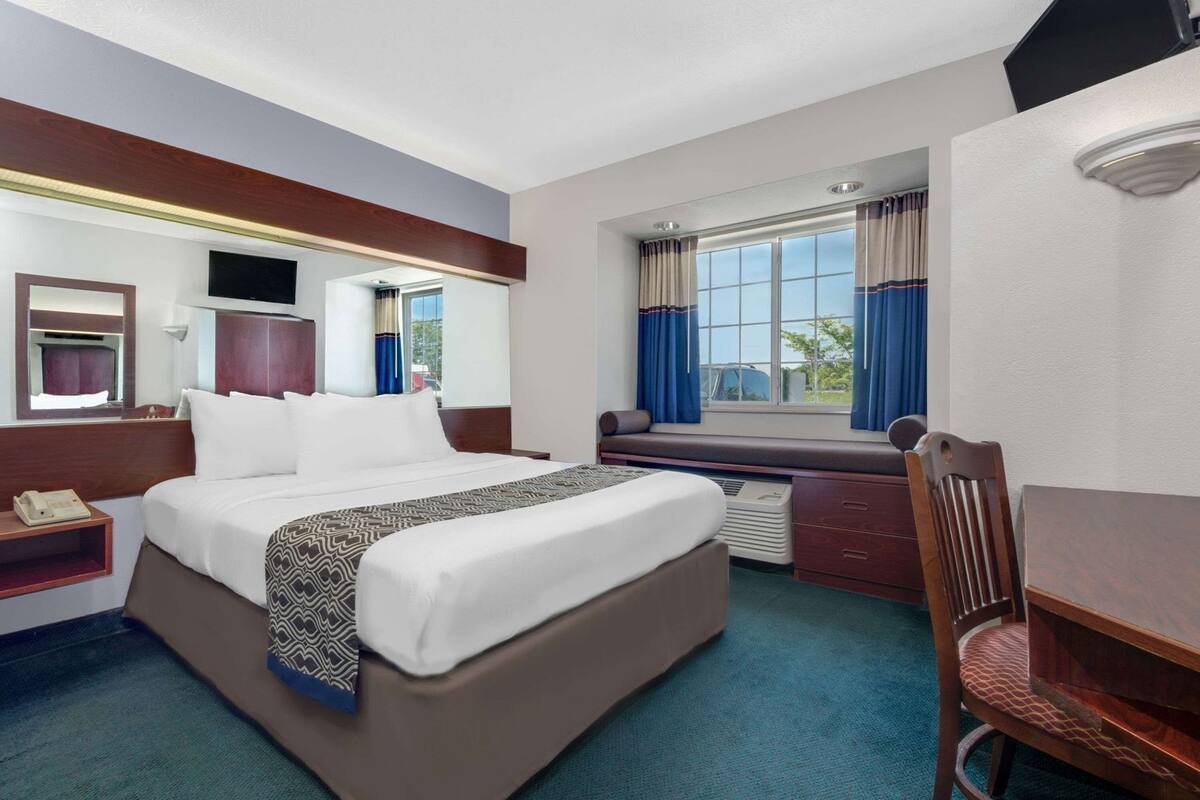 A hotel room with a large bed, a desk, a chair, a TV, a window with curtains, and a mirror.
