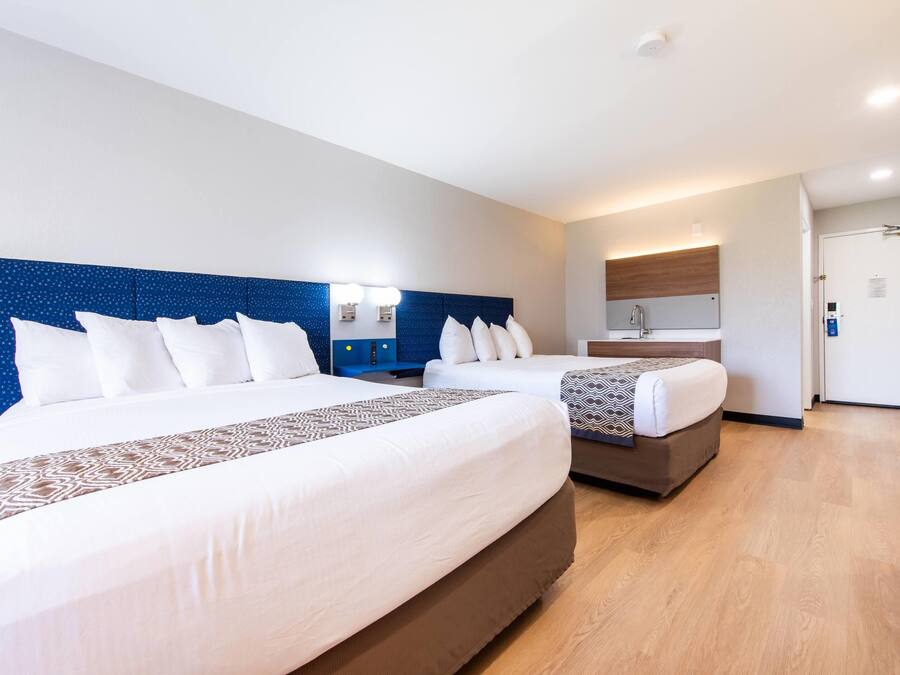 Habitación de hotel con dos camas, kitchenette pequeña, baño y puerta.