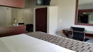 A hotel room with a bed, a desk, a chair, a wardrobe, a television, and a mirror.