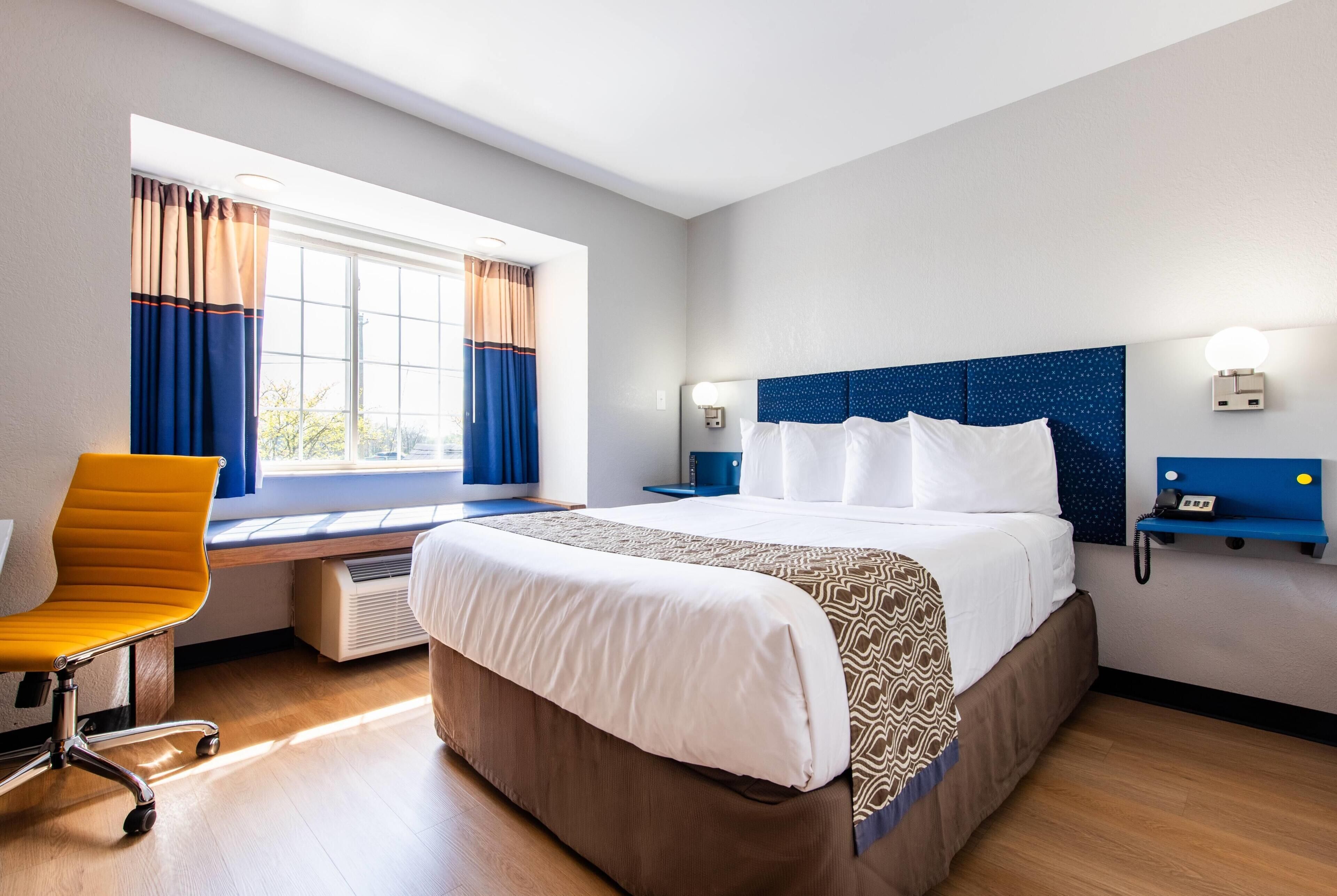 Een hotelkamer met een groot bed, een bureau, een stoel, een raam met gordijnen en een aan de muur bevestigde telefoon.