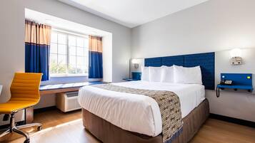 Een hotelkamer met een groot bed, een bureau, een stoel, een raam met gordijnen en een aan de muur bevestigde telefoon.