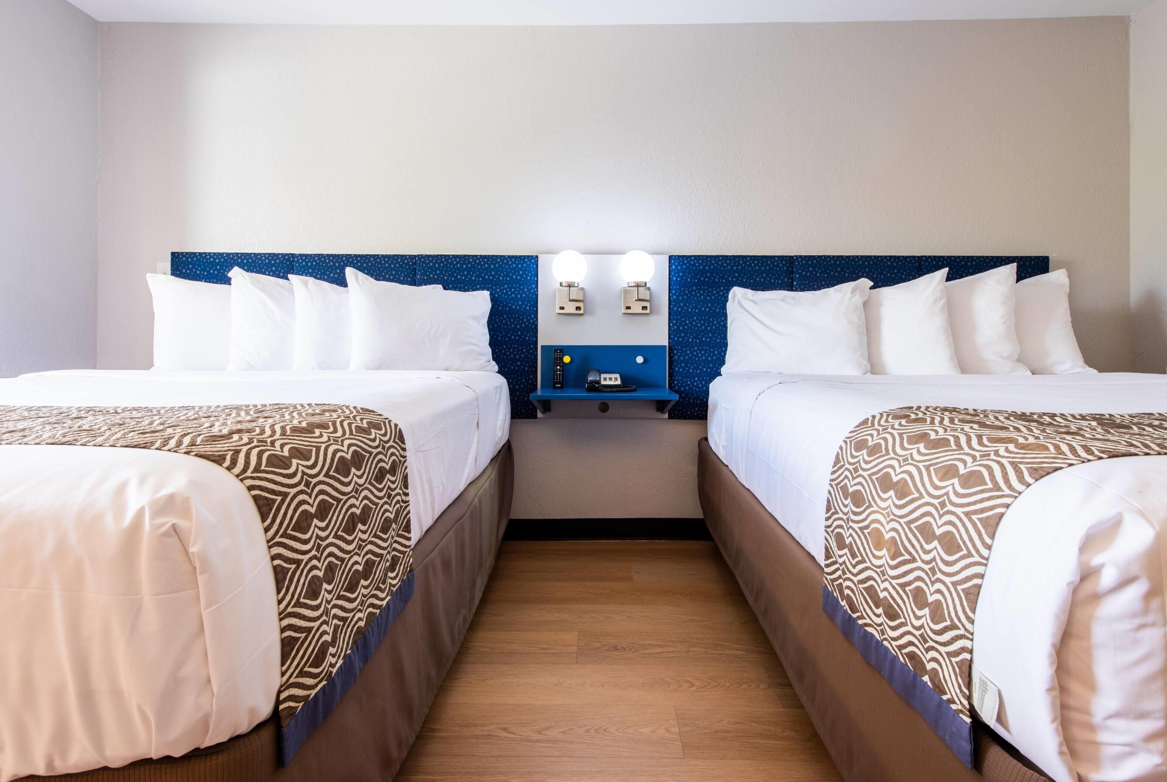 Ein Hotelzimmer mit zwei Betten, einem Nachttisch mit Lampe und einem blauen Kopfteil.