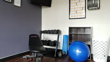 Un gimnasio con equipo de ejercicio, un reloj de pared, un televisor y un tablón de anuncios.