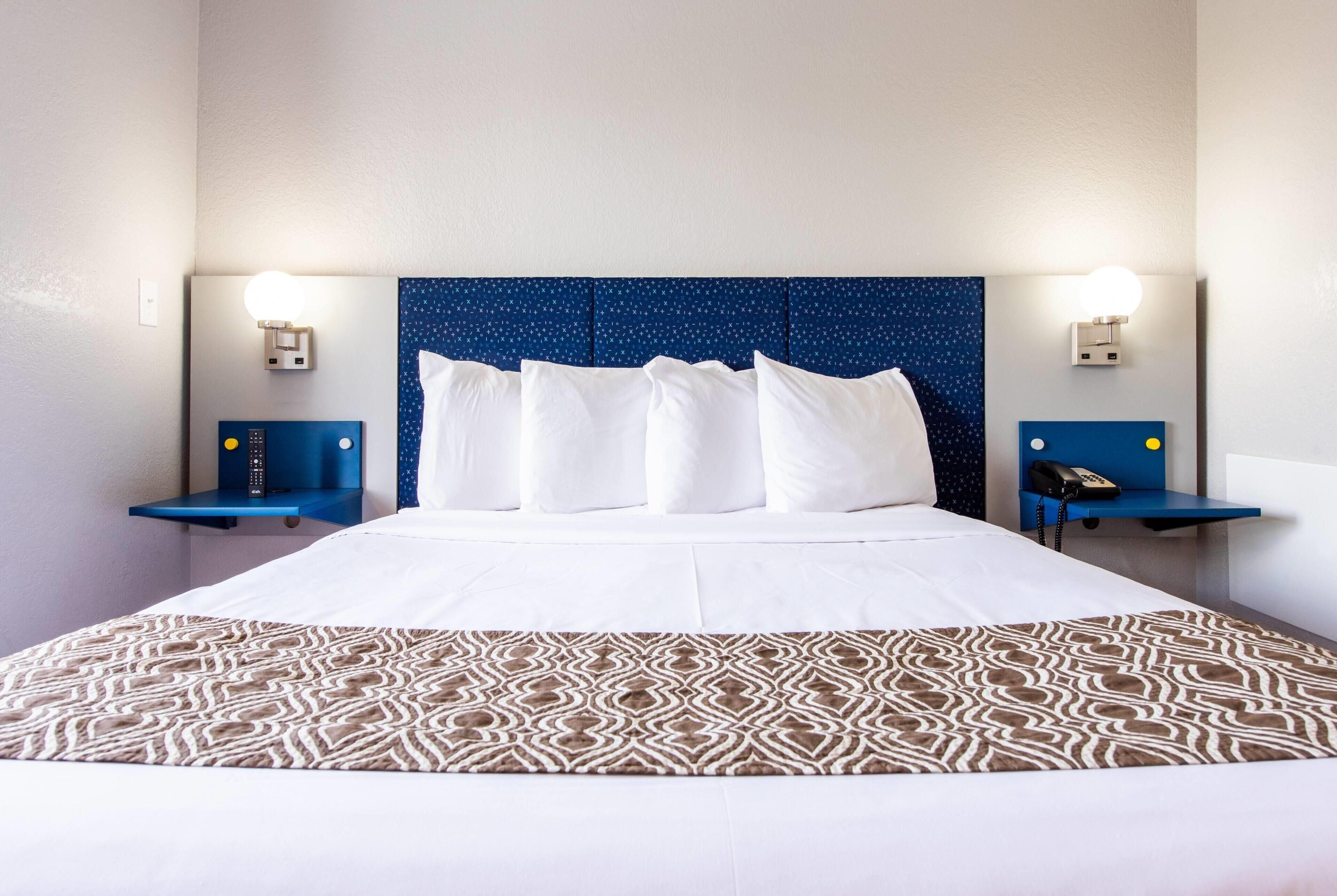 A hotel room with a large bed, two bedside tables with lamps, a patterned bedspread, and a blue headboard.