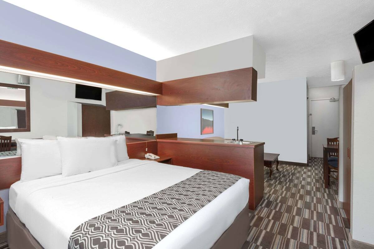 A hotel room with a bed, a desk, a chair, a mirror, and a bathroom door.