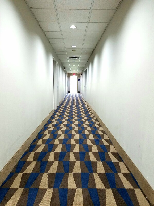 A long, narrow hallway with a patterned carpet and white walls. - Microtel Inn & Suites by Wyndham London (London)