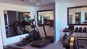 A gym with treadmills, elliptical machines, a bench, and free weights.