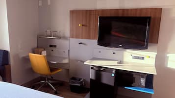 Una habitación de hotel con escritorio, una silla, televisor, microondas y cesto de basura.