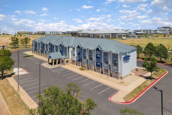 A hotel with a modern design, featuring a parking lot and a landscaped area with trees.