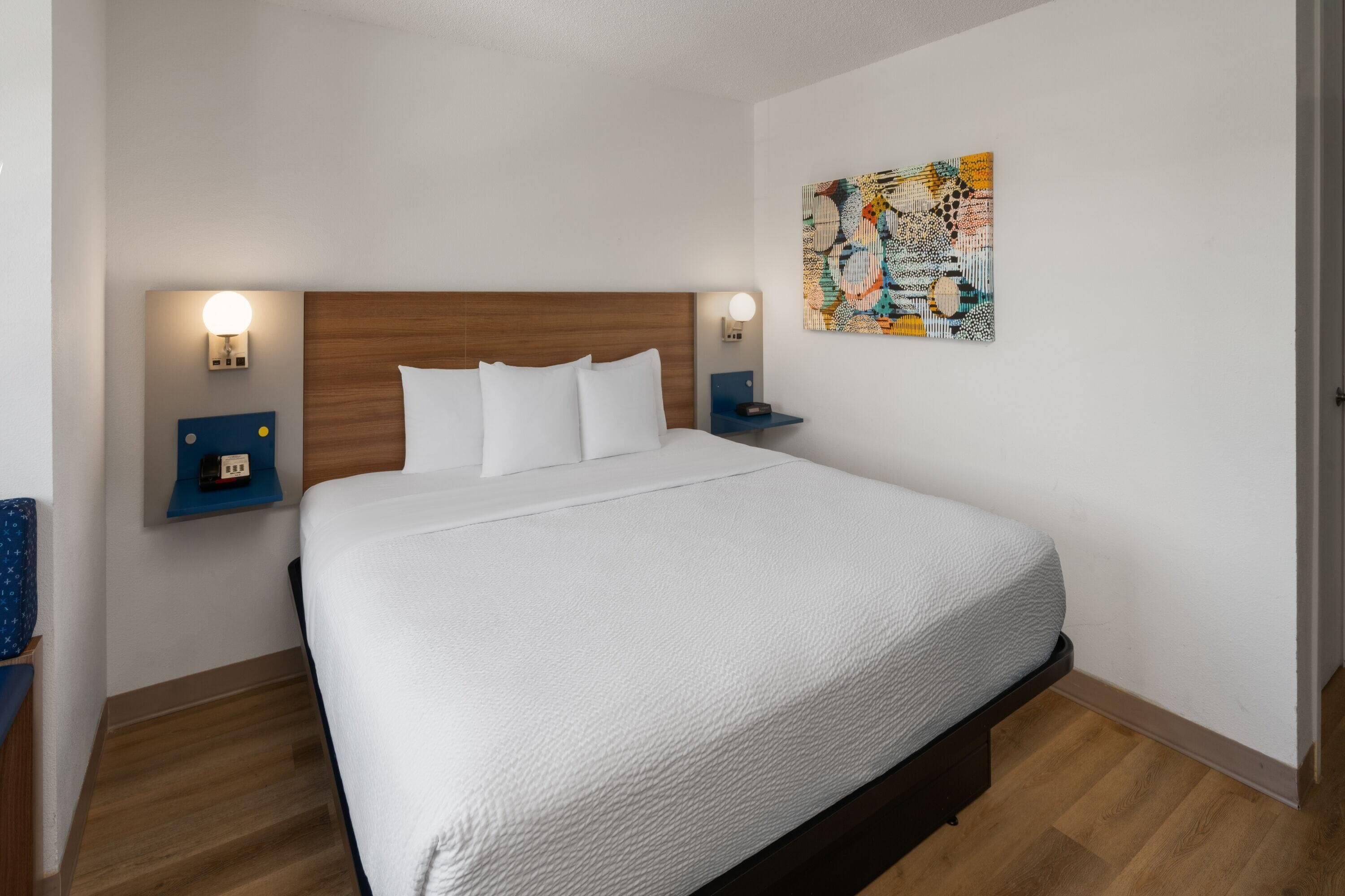 Une chambre d’hôtel avec un grand lit, deux tables de chevet, une œuvre d’art accrochée au mur et un plancher en bois.