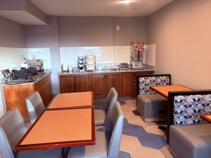 A modern kitchen with a coffee machine, toaster, and kettle. There are two dining tables with chairs.