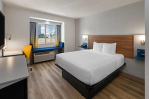 A hotel room with a bed, a desk, a chair, a window with curtains, and a wall-mounted lamp. - Microtel Inn & Suites by Wyndham Denver Airport (Denver)